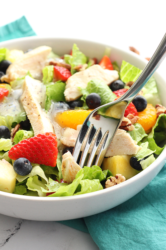 white bowl filled with salad that is topped with fresh fruit and chicken.