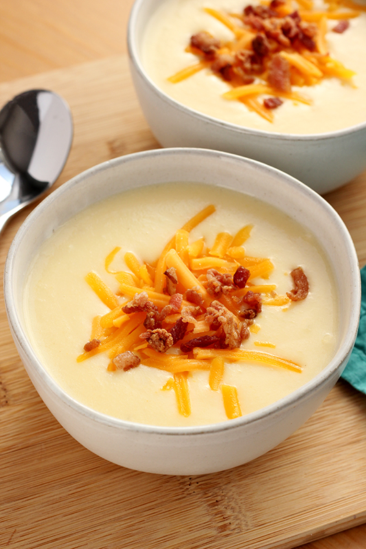 close up of cauliflower soup in a white bowl topped with cooked bacon and cheese