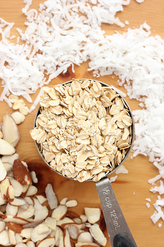 measuring cup filled with oats with shredded coconut and sliced almonds on a table