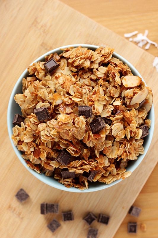 Top down image of a bowl filled with granola sitting on top of a wooden cutting board