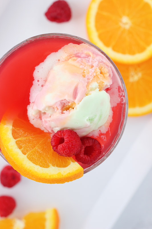 close up of a glass filled with punch and sherbet ice cream with fresh fruit garnish