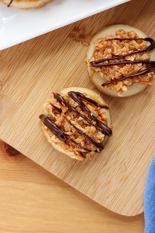 two Samoa cookies on a wooden cutting board
