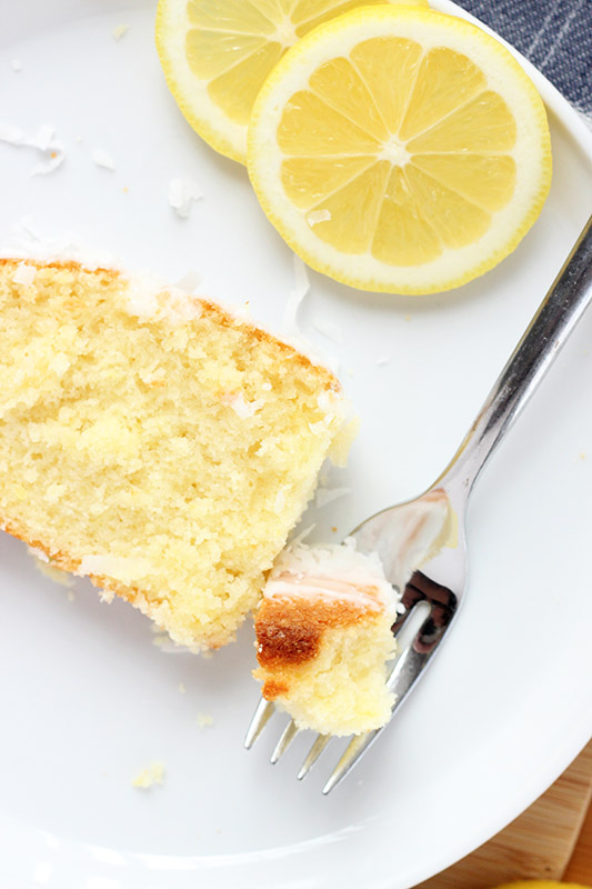 close up image of a bite of lemon loaf with lemon slices on a white plate