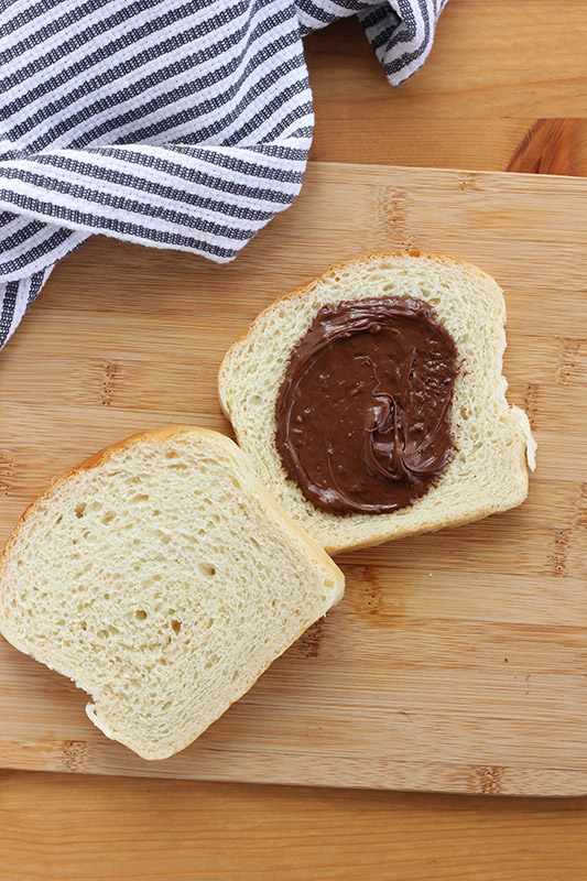 two slices of bread, one spread with nutella, on a wooden cutting board