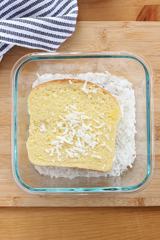 French toast slice dipped in egg sitting on top of a bowl of shredded coconut