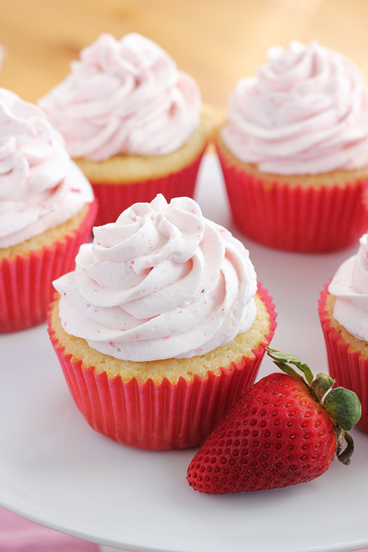 strawberry shortcake cupcake in a pink wrapper with whipped cream and fresh berry