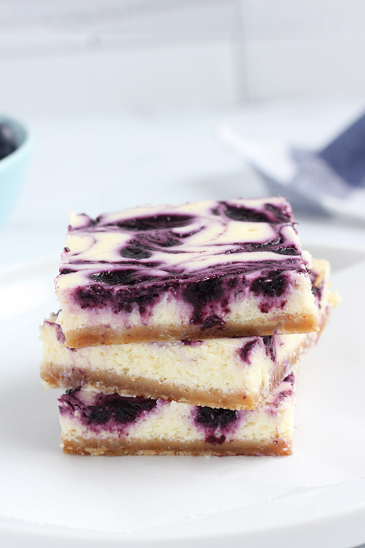 three blueberry cheesecake bars stacked on a white plate