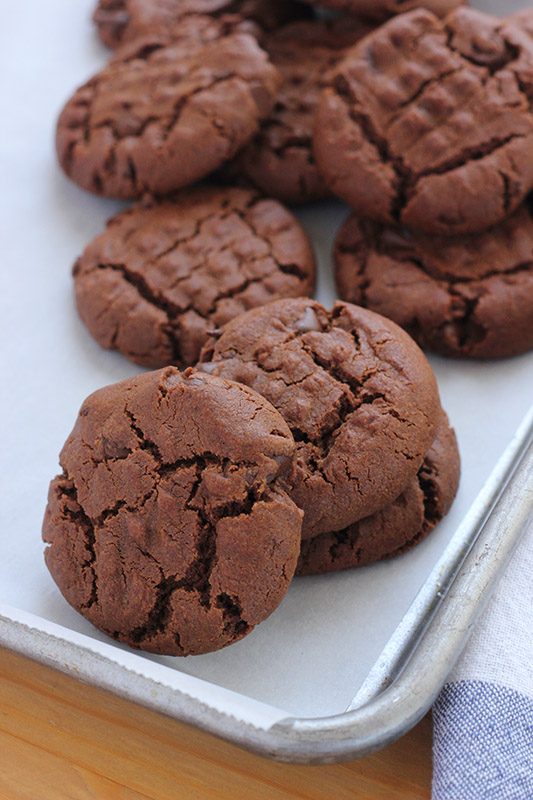 Baking tray lined with parchment paper and stacked with chocolate peanut butter cookies