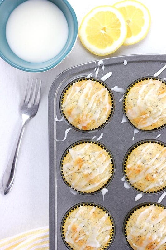 Close up image of muffins that are baked and sitting inside a tin with a drizzle of icing