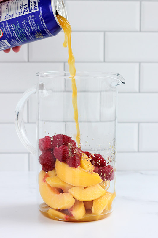 peach nectar being poured into a pitcher with raspberries and peaches
