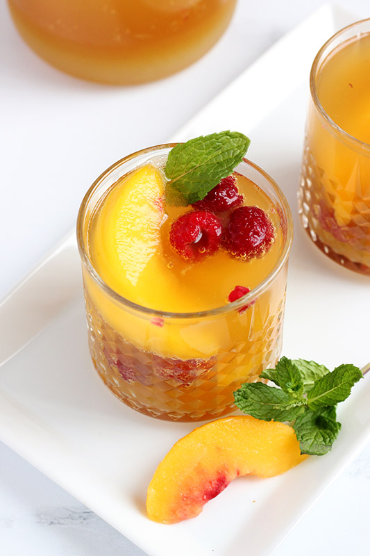 glass filled with sangria and fresh peaches and raspberries