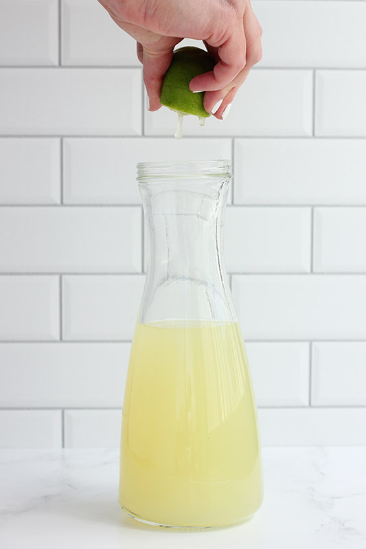 lime being squeezed into a tall jar of juice