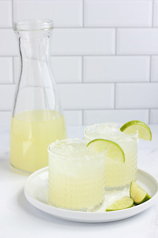 pitcher filled with margarita with two glasses and sliced limes