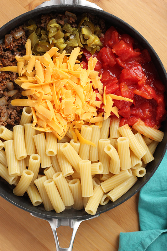 Pan filled with taco pasta ingredients on a wooden table with a teal napkin on the side