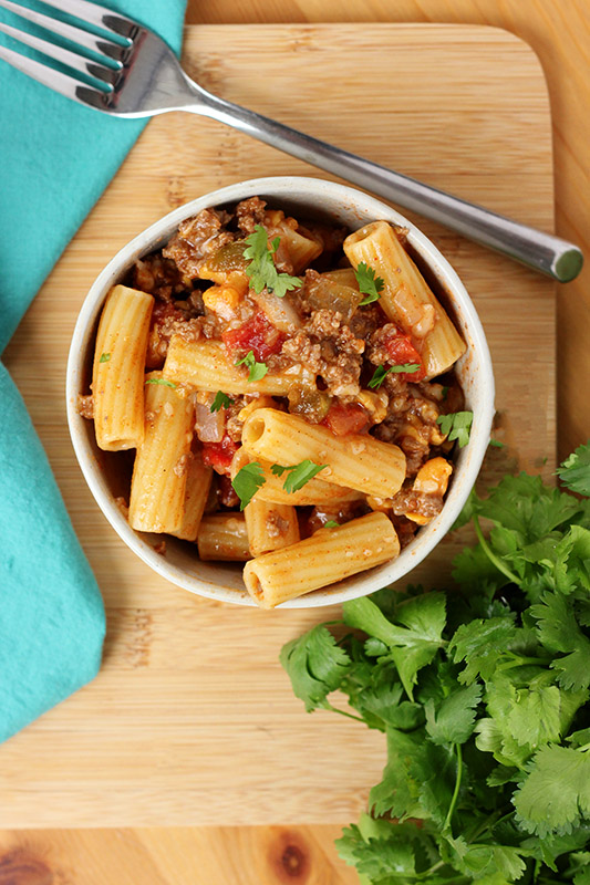 bowl of pasta sitting on a wooden cutting board with a side of cilantro 