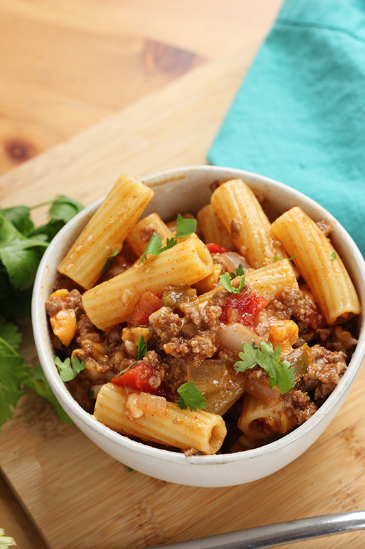 close up image of a white bowl filled with pasta and a bunch of cilantro on the side