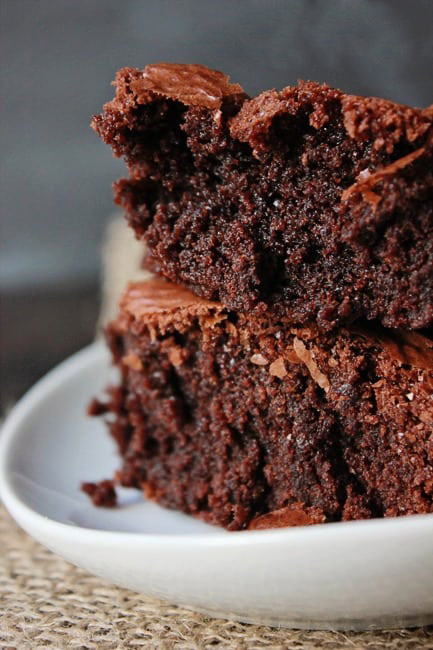 close up photo of two brownies stacked on a white plate