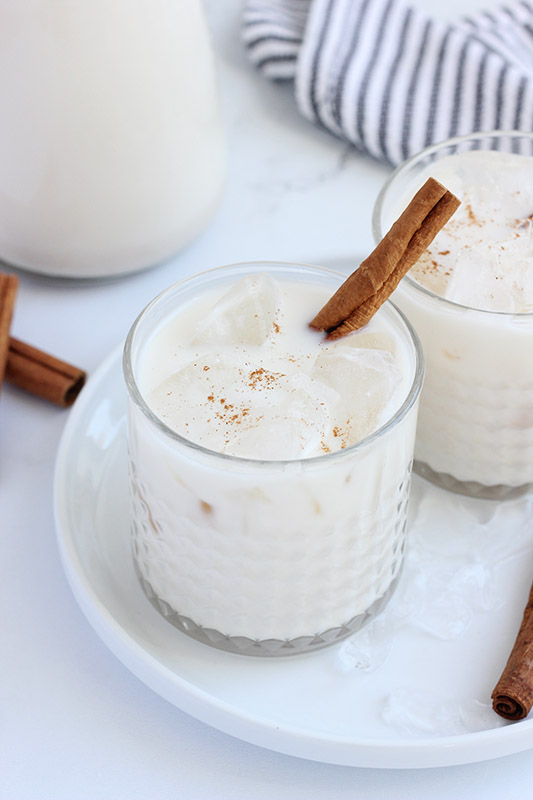 glass of horchata on a white plate with a cinnamon stick