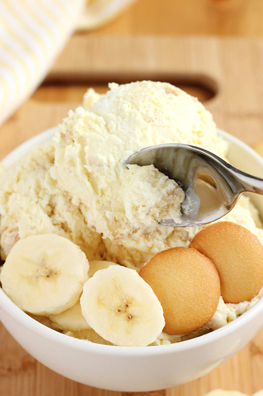 white bowl filled with ice cream, banana slices, and vanilla wafer cookies with a spoon being scooped into the ice cream