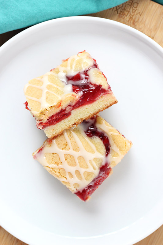 two cherry bars on a white plate topped with frosting drizzle