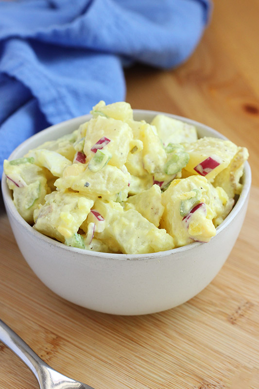 close up image of chopped potatoes in a salad inside an off white bowl