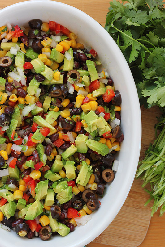 bowl of avocado salsa sitting on a wooden cutting board with cilantro bunch on the side