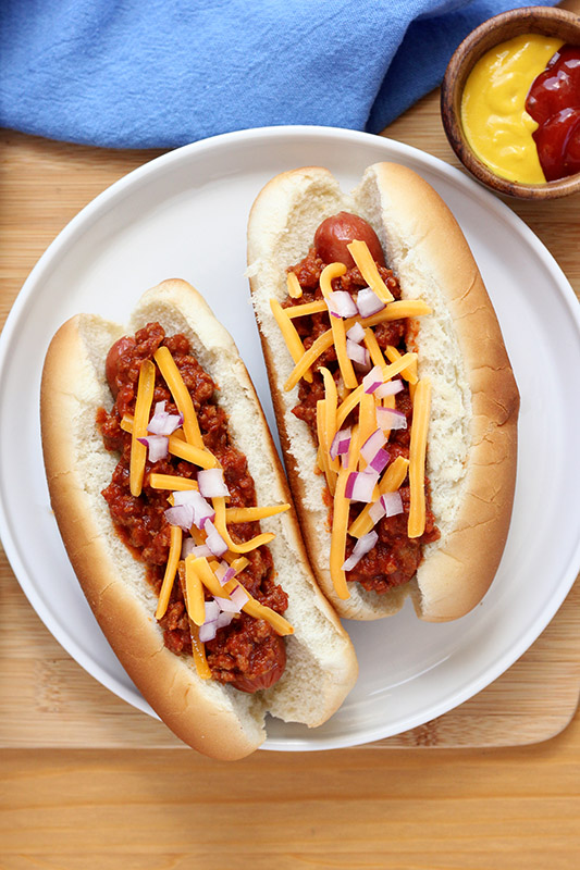 two hot dogs in buns topped with chili, cheese, and onions