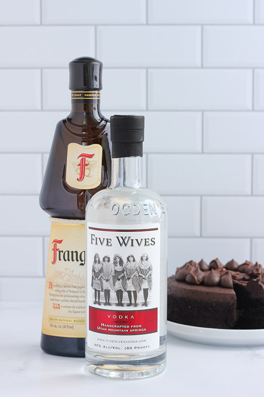 bottles of vodka, frangelico and chocolate cake on a white table
