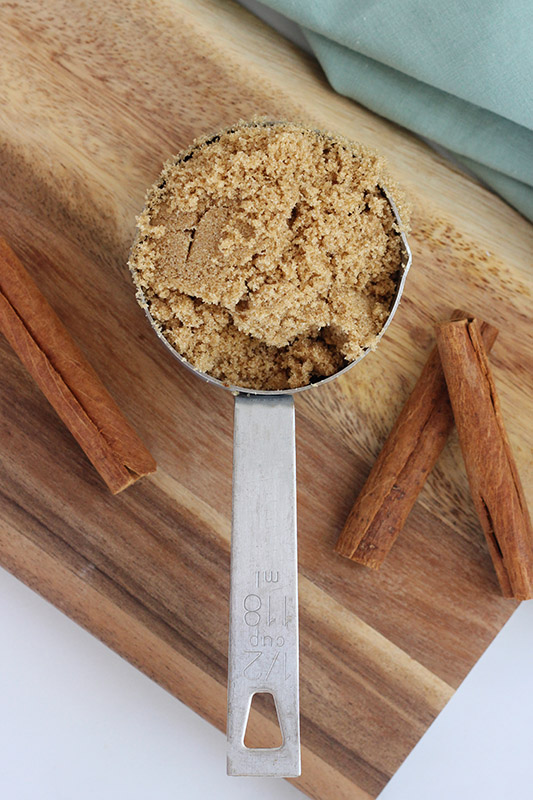 brown sugar in a measuring cup with cinnamon sticks on a wooden cutting board. 