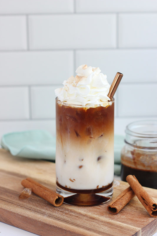 glass filled with coffee and milk topped with whipped cream and a gold straw