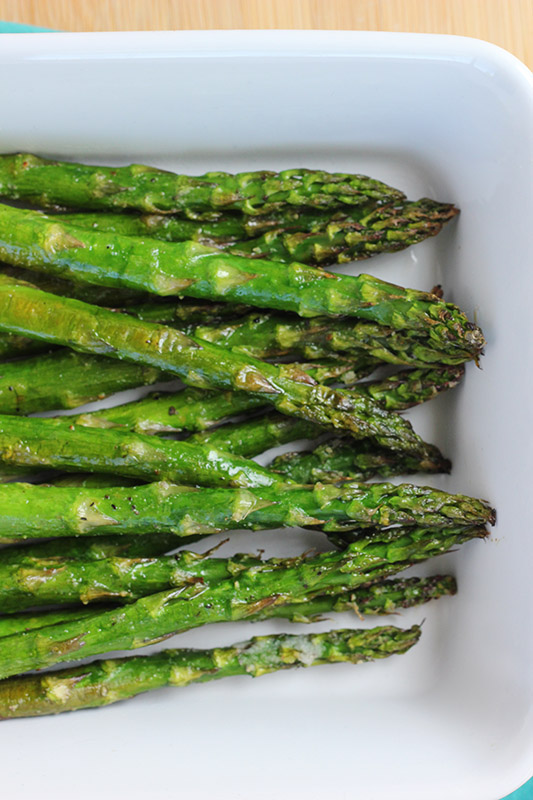 close up of a pile of cooked asparagus in a white serving dish