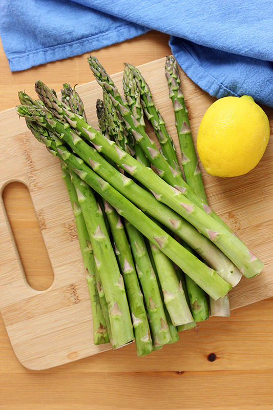 stack of fresh asparagus with a lemon slice on a wooden cutting board