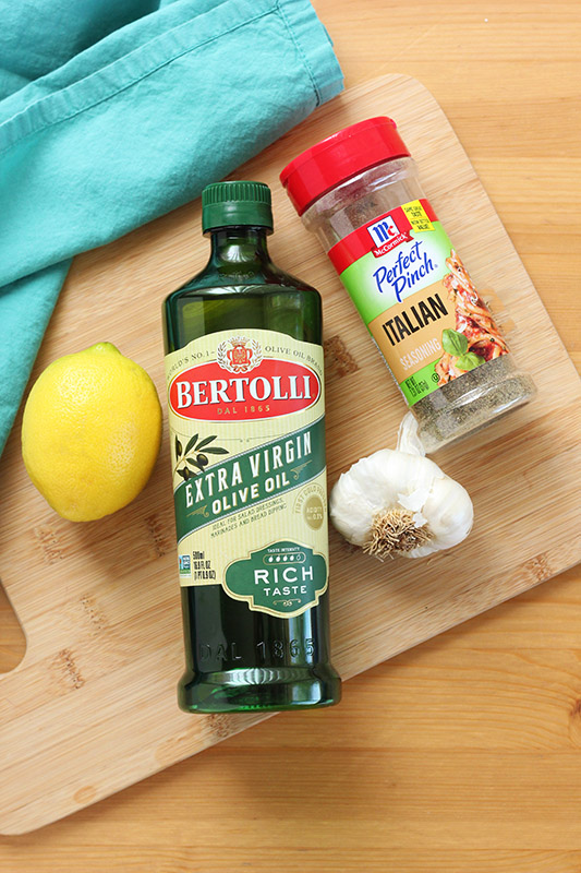 olive oil, garlic, italian seasoning, and a lemon on a wooden cutting board