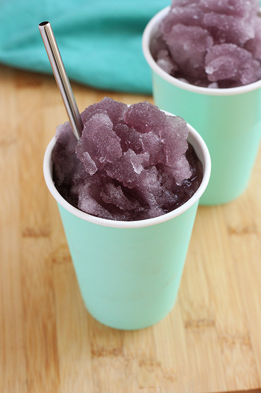 grape slush in a teal paper cup on a wooden cutting board