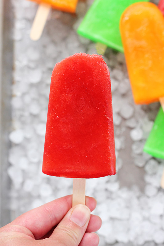 hand holding a single cherry popsicle over a tray of ice