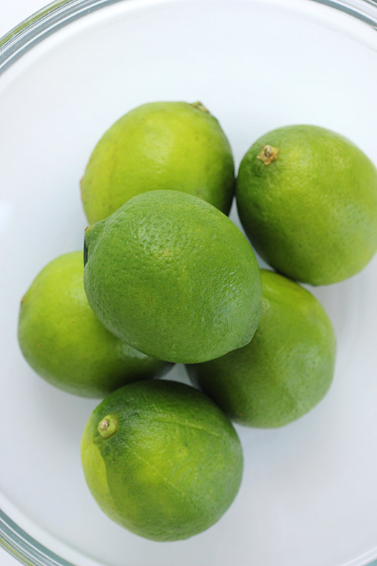 Glass Bowl filled with limes on a white surface