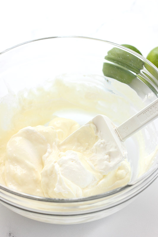 Glass bowl filled with cream cheese and sweetened condensed milk being stirred with a white spatula.