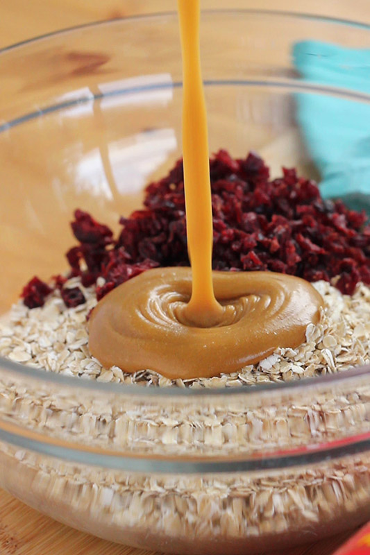 peanut butter sauce being poured into a bowl of oats and cranberries