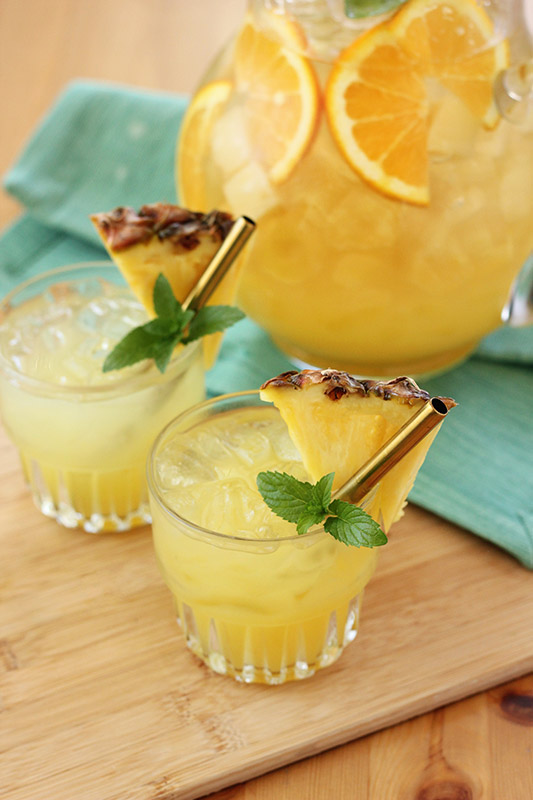 two glasses filled with pineapple punch, fresh pineapple slices and mint