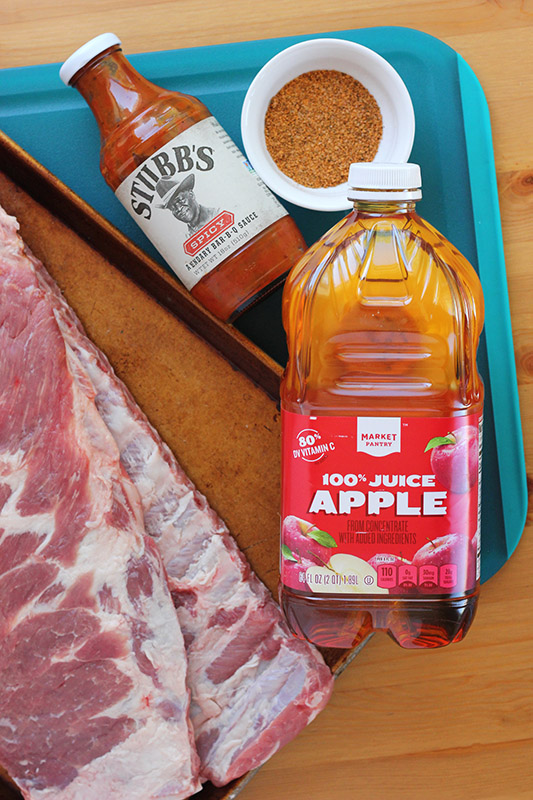 large cutting board stacked with uncooked ribs, bbq sauce, seasoning and apple juice
