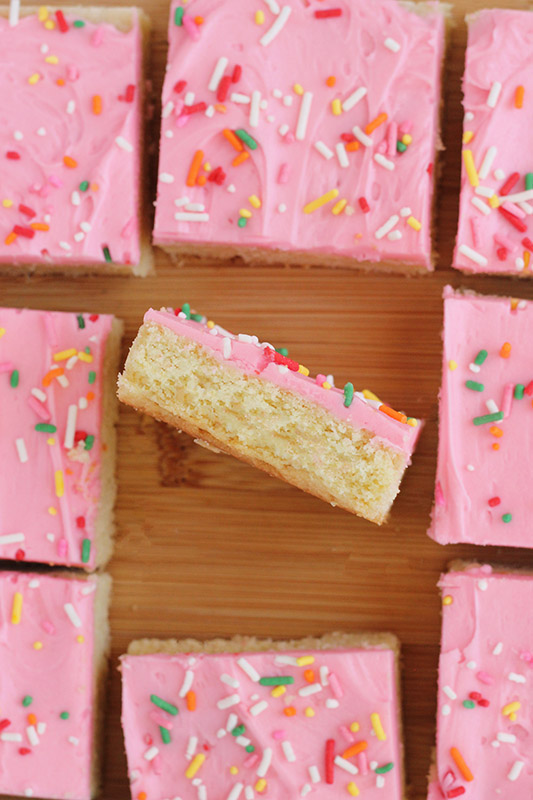 frosted sugar cookie bars layered in a line on a wooden cutting board with one turned on its side