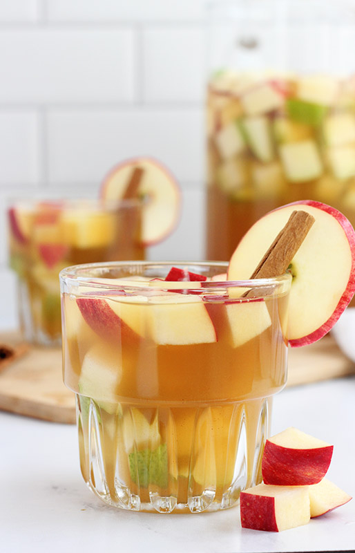 close up image of a clear glass filled with apple cocktail and apple slices