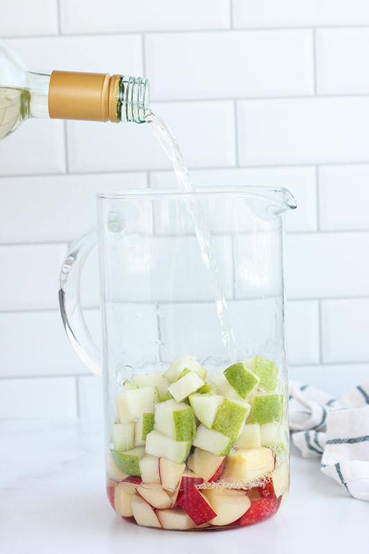 wine being poured into a pitcher with apple slices