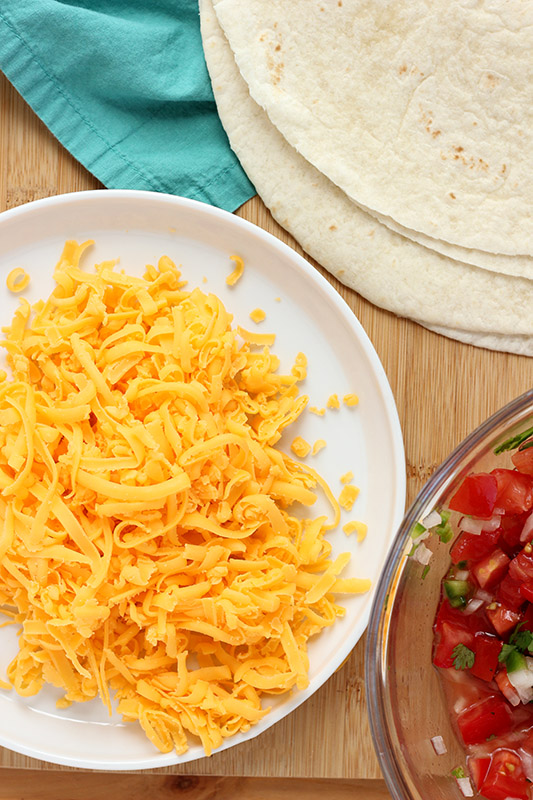 shredded cheese, tortillas, and pico on a cutting board