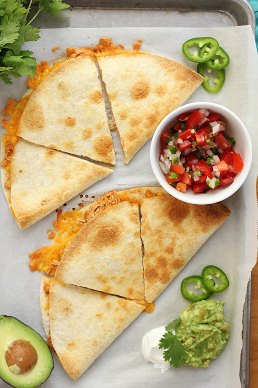 cheese quesadillas sliced into triangles on a sheet pan with pico and jalapenos 
