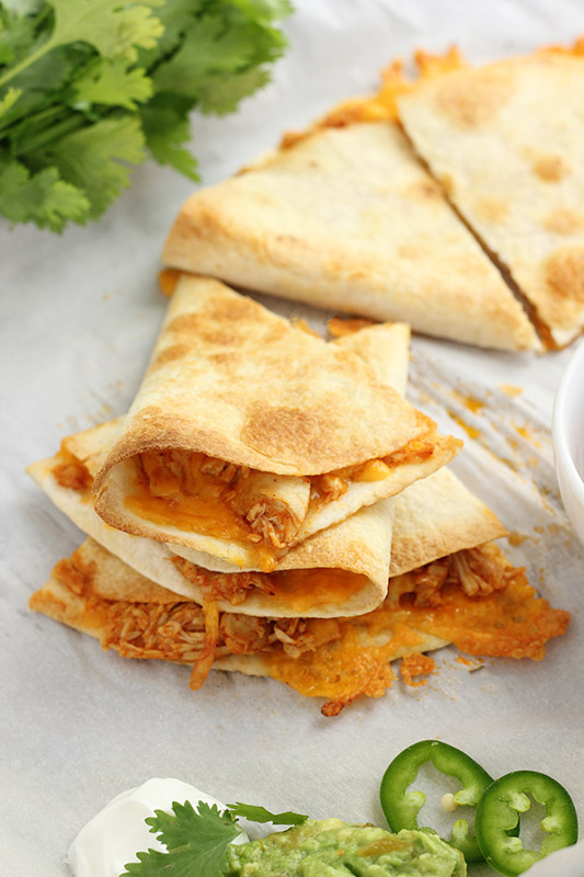 quesadilla triangles stacked on top of each other on a parchment lined baking tray