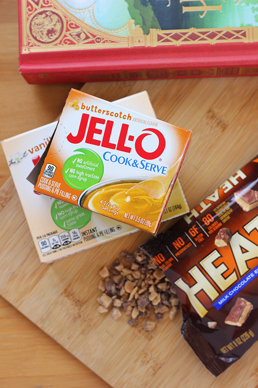 cookie ingredients including box of jello and toffee bits on a wooden cutting board