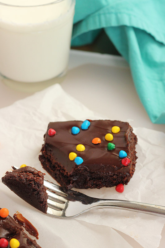 brownie topped with candy pieces sitting on a piece of parchment with a bite on a fork