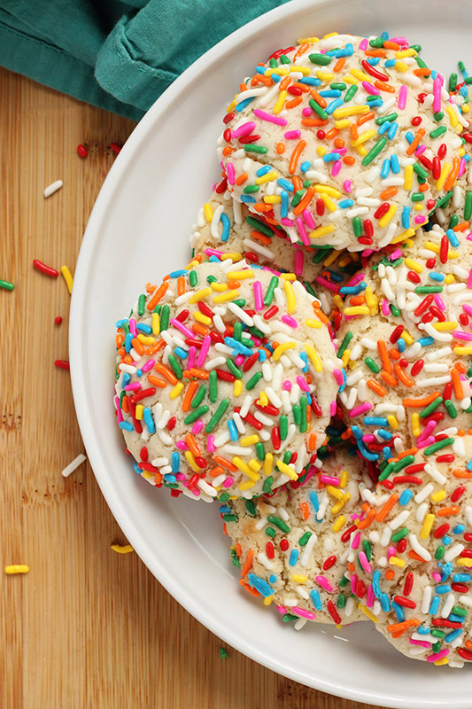 white plate stacked with cookies rolled in rainbow colored sprinkles