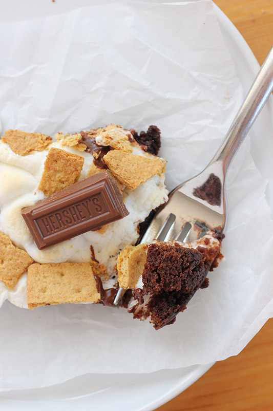 close up image of a brownie that is topped with melted marshmallows and graham pieces with one bite on a fork